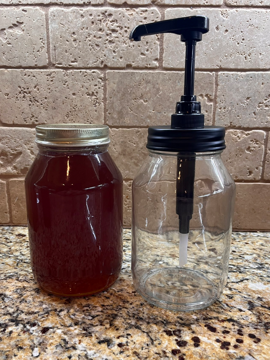 honey pump in glass jar of honey next to a full honey jar