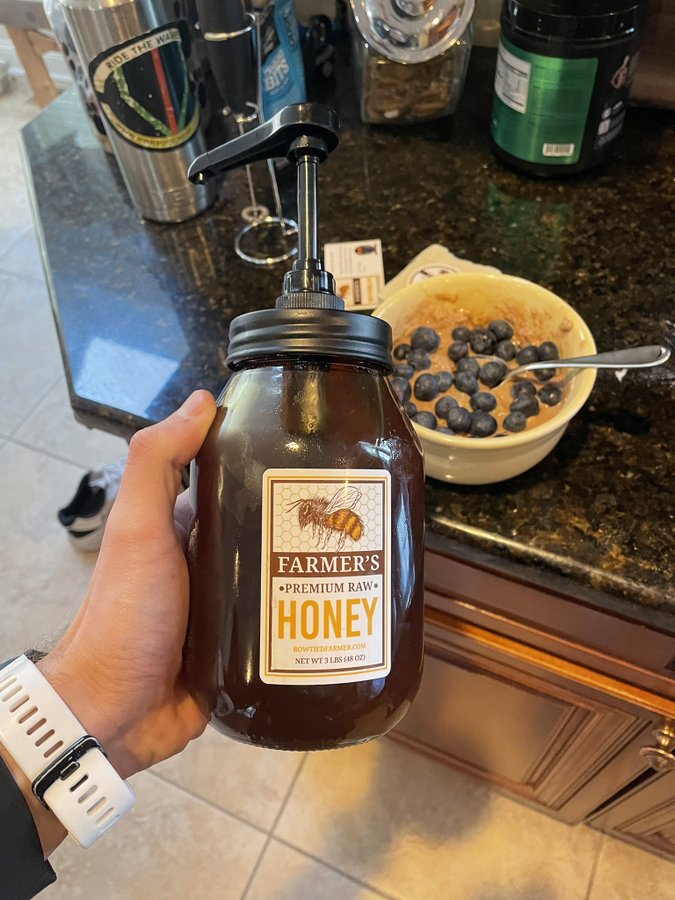 hand holding no mess honey with breakfast of blueberries and honey oatmeal in background